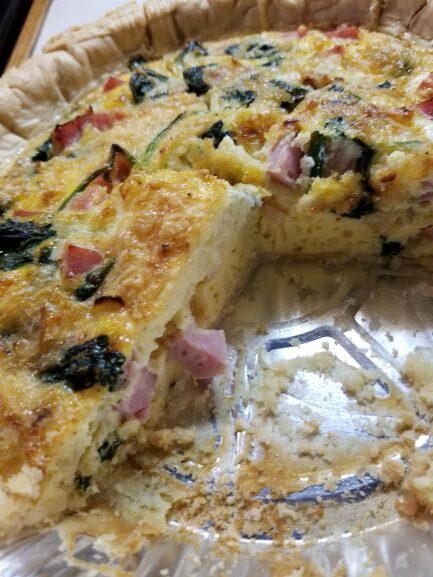 Spinach and Ham Quiche with slice out of pie plate so you can see the filling