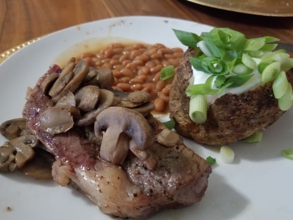 Grilled Cowboy Cut Rib Eye Steaks plated with baked beans and baked potato with butter, sour cream, and chives