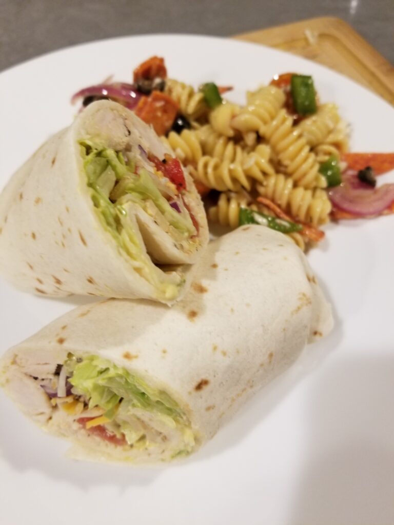Chipotle Turkey and Cheddar Wraps cut in half on a white plate with pasta salad.